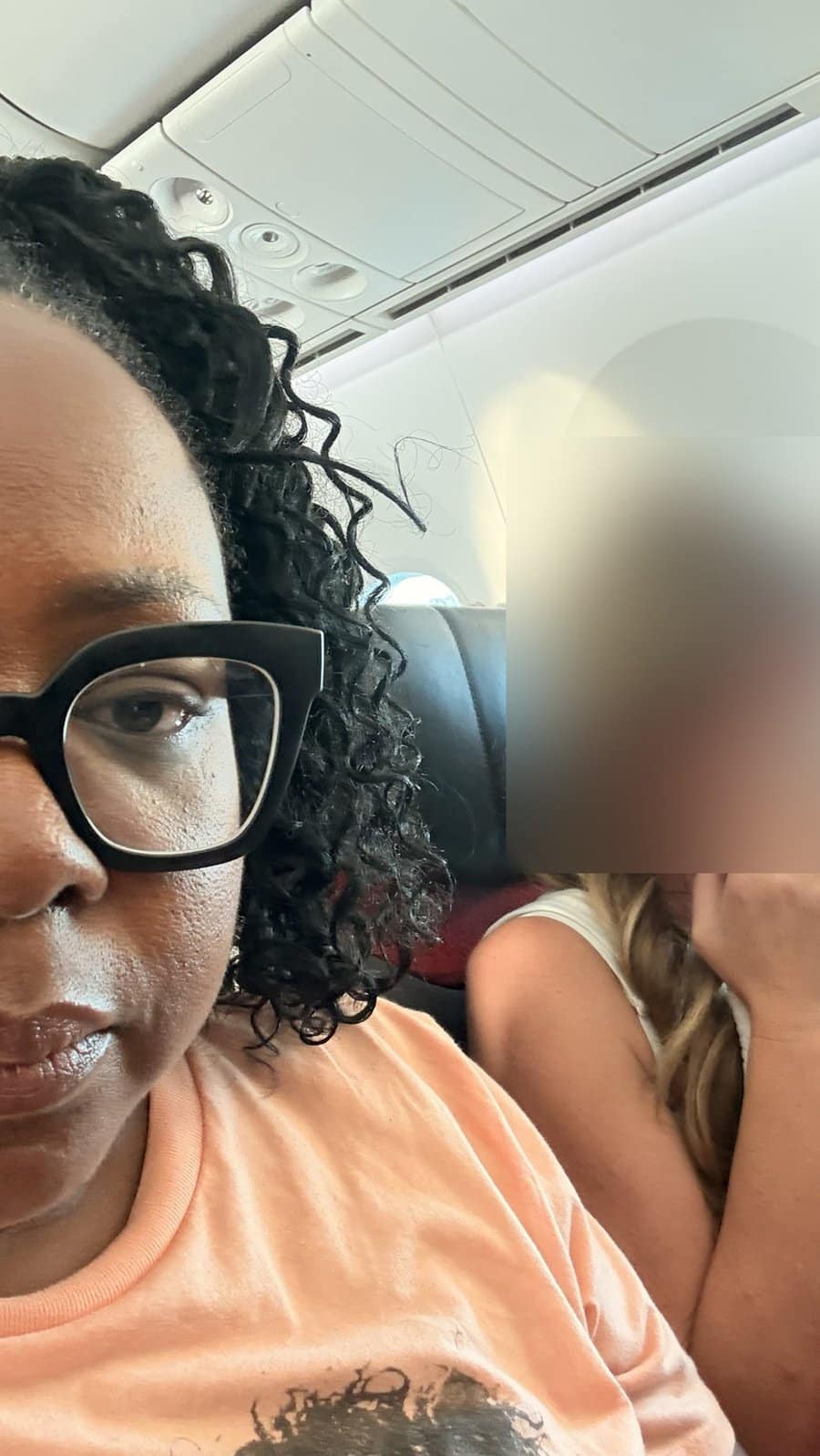 Tomiko Harvey in her aisle seat while the seatmate who asked her to switch seats on a plane covers her face, blurred for privacy